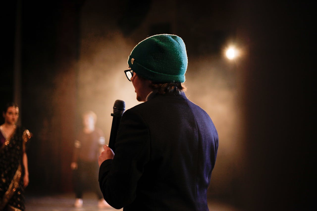 Moody scene of a performer holding a microphone under a spotlight on stage.