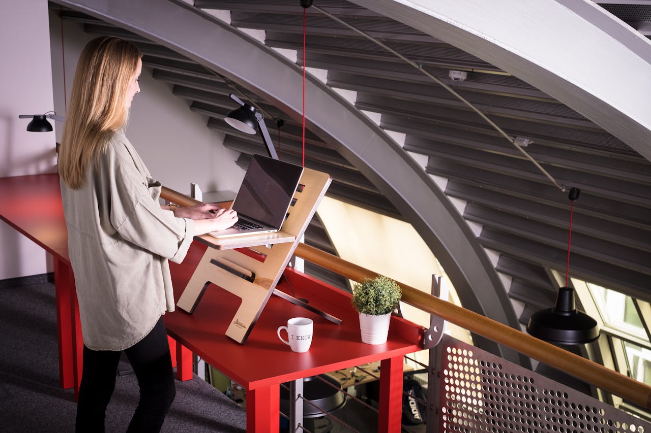 Woman using a laptop on a standing desk indoors in a creative workspace.