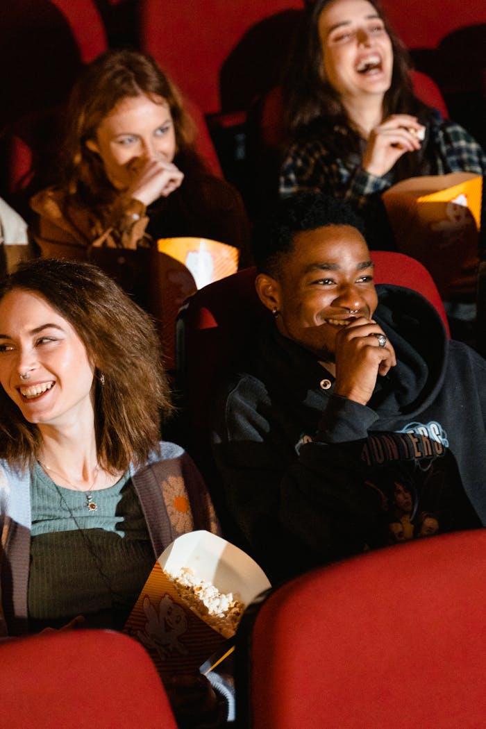 services-bg Group of diverse friends laughing and enjoying popcorn while watching a movie in a theater.